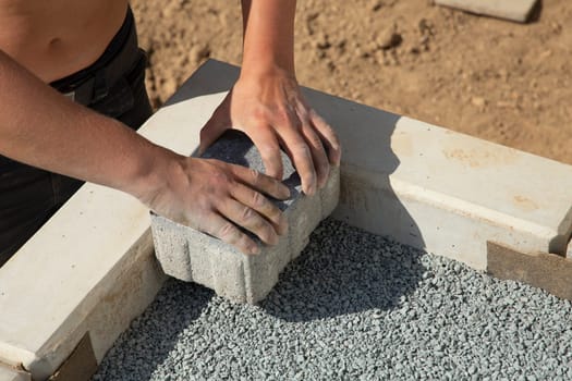 A gloved craftsman lays down the paving stones in layers. Laying gray concrete paving slabs in the courtyard of the house on a sandy foundation.