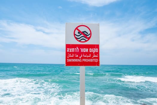 swimming forbidden in english and hebrew at a sign at the beach in Tel Aviv, Israel
