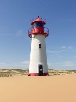 Lighthouse on sand dune against blue sky with white clouds on northern coast of Sylt island near List village, Germany