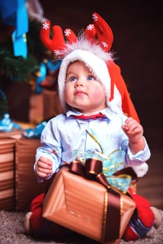 A child with a Christmas gift in a deer costume is sitting on the floor in the studio in close-up