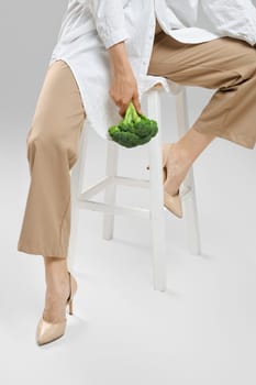 Daily healthy eating concept. Cropped image of woman sitting on chair with broccoli in hand