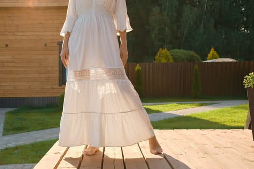 Barefoot legs of a woman visible through a thin dress. Unrecognizable woman on terrace of tiny house
