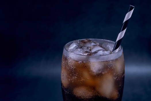 Cool glass of cola drink with ice, bubbles and fizz. Fresh cold sweet with ice cubes. Cola glass with summer refreshment on black.