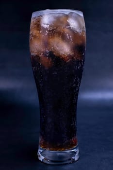 Cool glass of cola drink with ice, bubbles and fizz. Fresh cold sweet with ice cubes. Cola glass with summer refreshment on black.