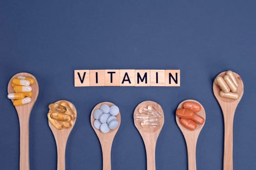 Different vitamins in wooden spoons with text on gray background. Pills, drugs, supplements, medicine, pharmacy and healthcare concept.