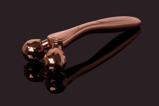 Skin care tools. A golden metal 3D face massager, face lift roller for better blood circulation and muscle activation on dark background. Beauty, skin treatment concept.