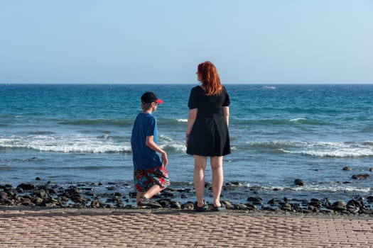 Young girl with a short black dress and a boy with shorts and a cap on a promenade by the sea, with blue sky,Young girl with a short black dress and a boy with shorts and a cap on a promenade by the sea, with blue sky