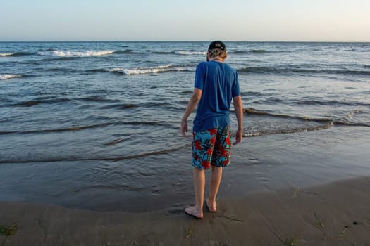 A boy wearing shorts and a cap stands on a sandy beach by the sea, with a blue sky,A boy wearing shorts and a cap stands on a sandy beach by the sea, with a blue sky