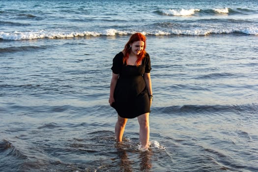 Young girl in black short summer dress stands in the waves on the sandy beach,Young girl in black short summer dress stands in the waves on the sandy beach
