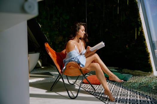 Young sensual woman relaxing in lounge chair of home backyard and reading a book during sunny summer day