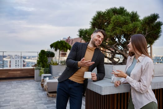 Business colleagues chitchatting during coffee break at office roof terrace. Man and woman coworkers having nice conversation sharing ideas emotionally speaking at balcony