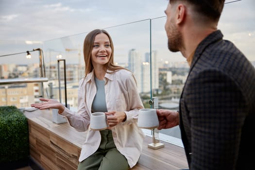 Man and woman coworkers having nice conversation sharing ideas emotionally speaking at balcony. Freelancers team taking coffee break during workday in office