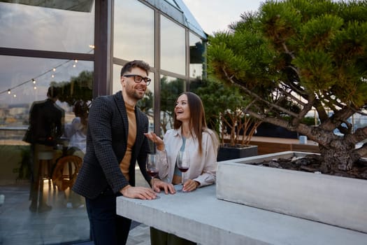 Young man and woman business colleagues talking drinking wine during corporate rooftop party. Teambuilding and social gathering