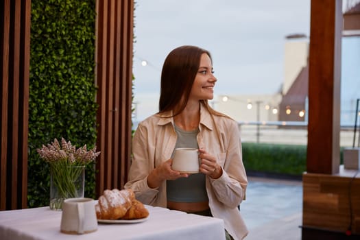 Young attractive woman sitting at table drinking coffee in cafe. Freelance occupation and remote work enjoyment