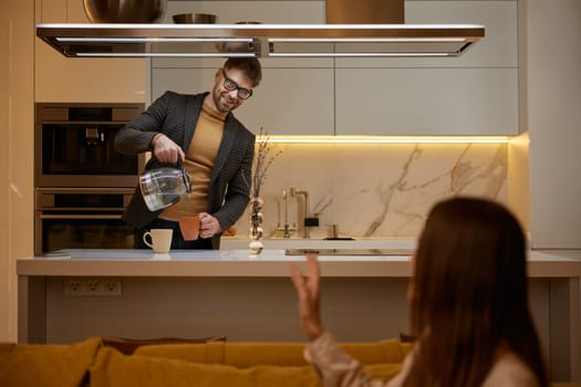 Attentive husband standing at counter desk in home kitchen and cooking tea for loving wife. Family people relationship concept