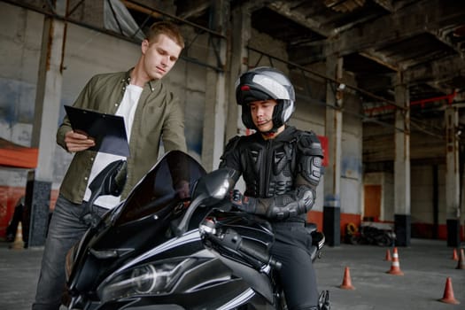 Personal lesson at motorcycle school concept. Male instructor teaching young biker explaining important things before start to move