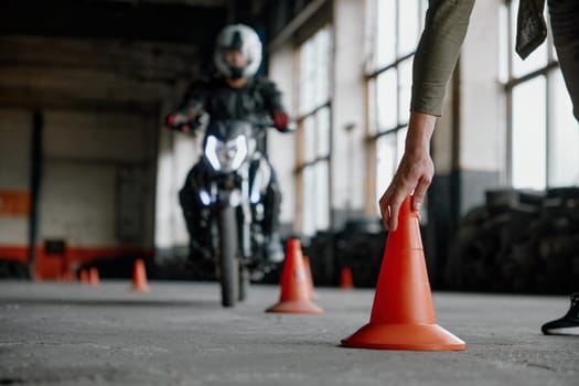 Motorbike driving school lesson with instructor putting cone on track front of student. Indoor moto drome training center