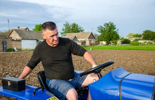 Kherson oblast, Ukraine - May 29, 2021: An elderly farmer sits and drives a tractor. Seasonal worker. Recruiting and hiring employees for work in farm. Milling soil. Loosening , cultivation. Plowing