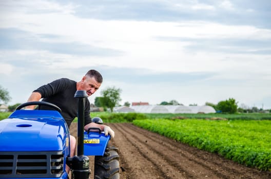 Kherson oblast, Ukraine - May 29, 2021: An elderly farmer drives a tractor on a farm. Milling soil, loosening ground before cutting rows. Preparation of land for future planting new crop.