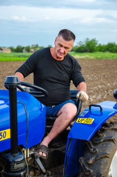 Kherson oblast, Ukraine - May 29, 2021: An elderly farmer sits and drives a tractor. Running a small agribusiness. Farming. Loosening, land cultivation. Mechanization in agriculture. Farm work.