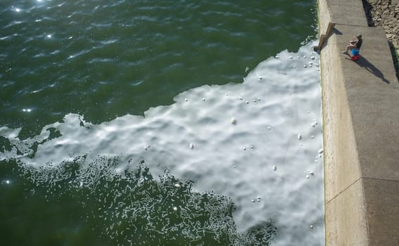 Man fishing at polluted river full of foam. Fish taken from polluted waters