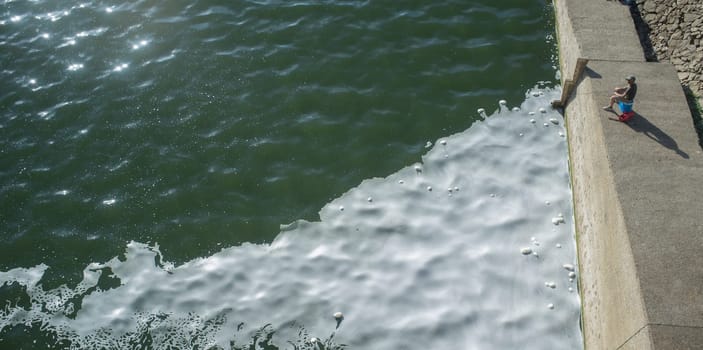 Man fishing at polluted river full of foam. Fish taken from polluted waters