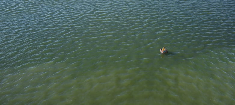 Float tube fisher floating over green waters of a reservoir. Long format