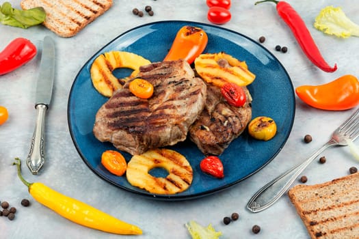 Grilled meat with pineapple rings, grilled steak and ananas on wooden table.