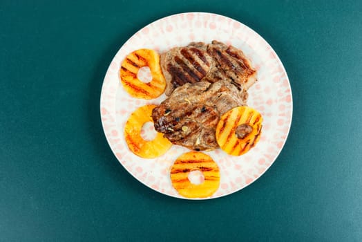 Grilled meat with pineapple rings, grilled steak and ananas on wooden table.