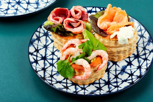 Puff pastry tartlets or canapes with fish, shrimp and bacon on a plate on the table.