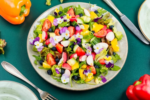 Spring salad of fresh vegetables decorated with edible flowers. Healthy salad.