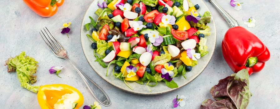 Spring salad of fresh vegetables decorated with edible flowers. Healthy salad.
