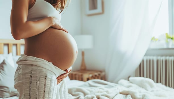 Beautiful pregnant woman holds hands on belly in bedroom at home. Young mother waiting of a baby. Concept of pregnancy, maternity, health care, gynecology, medicine. Close-up, indoors. Stylish boho interior beauty