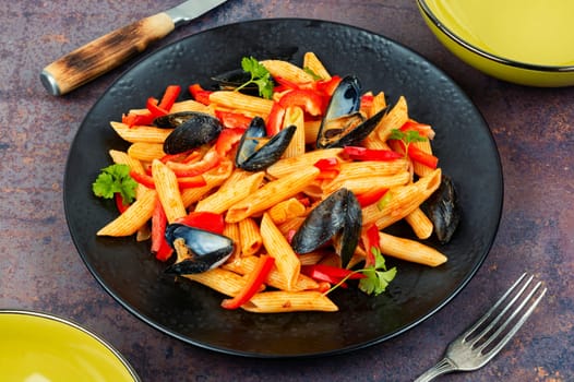 Macaroni with Atlantic mussels on a dark plate. Pasta with seafood. Noodles with mussels on wooden table. Top view.