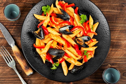 Macaroni with Atlantic mussels on a dark plate. Pasta with seafood. Noodles with mussels on wooden table. Top view.