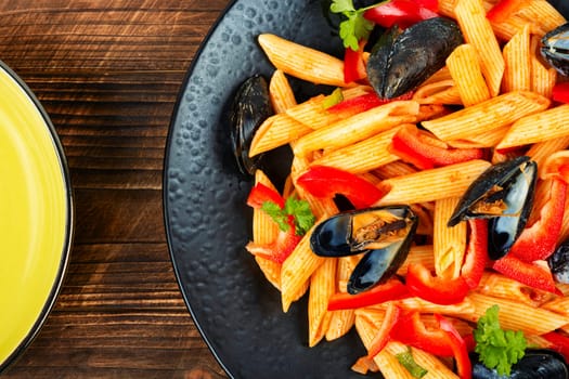 Macaroni with Atlantic mussels on a dark plate. Pasta with seafood. Noodles with mussels on wooden table. Top view.