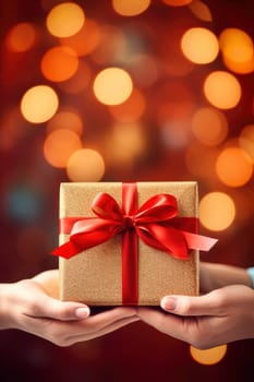 A person is holding a gift box wrapped in shiny red ribbon.