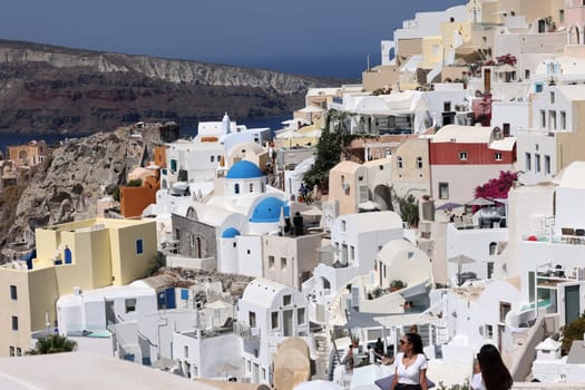 Oia, Santorini, Greece - July 3, 2021: Whitewashed buildings on the edge of the caldera cliff in Oia village, Santorini, Greece