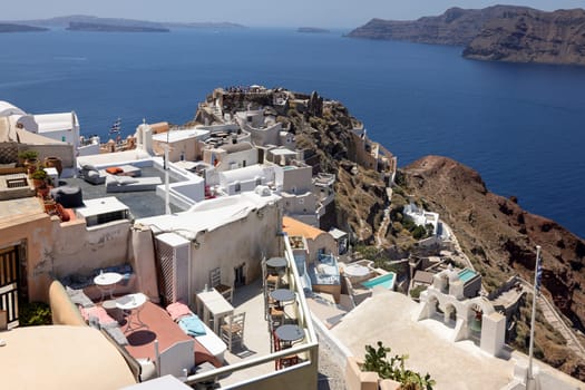 Oia, Santorini, Greece - July 3, 2021: Whitewashed buildings and the ruins of Castle of Agios Nikolaos on the edge of the caldera cliff, Oia village, Santorini, Greece