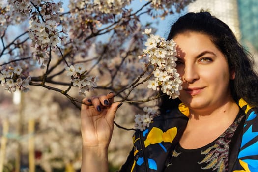 Young woman covering one eye with a branch of cherry blossoms in the park in spring.