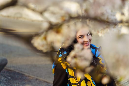 Young woman smiling while walking in blooming cherry blossom garden in spring.