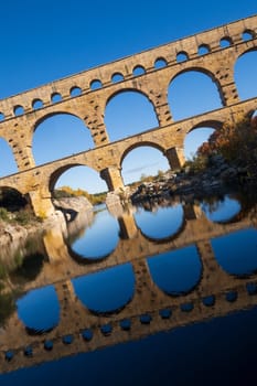 The Pont du Gard, photography composed in a modern style, tilted over blue sky. Ancient Roman three-tiered aqueduct bridge. Built in the 1st century AD to carry water to the Roman colony of Nemausus (Nîmes). Photography taken in Vers-Pont-du-Gard, Provence, southern France