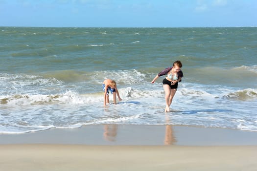 Two children have fun in the waves on the sea beach, Girl runs out of the water,Girl runs out of the water, boy plays in the waves