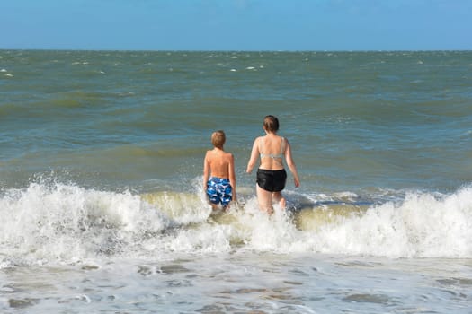 A boy and a teenage girl have fun in the waves on the sea beach