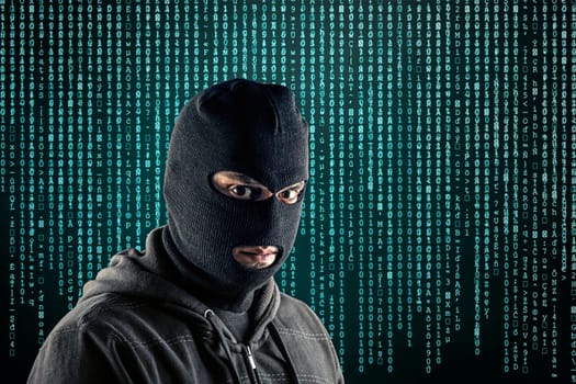 Criminal wearing black balaclava and hoodie over blue computer code background
