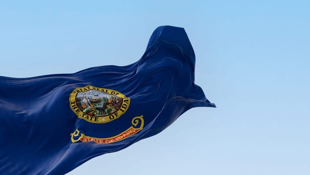 Idaho state flag fluttering in the wind. Blue background with the state seal and a red band with State of Idaho in gold text. 3d illustration render. Selective focus. Close-up