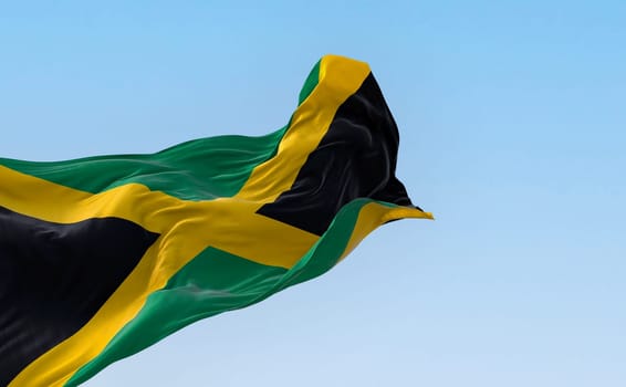 Jamaica national flag waving in the wind on a clear day. Gold saltire dividing it into four sections: two green and two black. 3d illustration render. Fluttering fabric. Selective focus