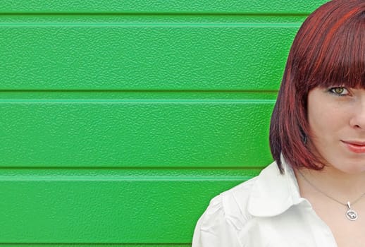 Half of the face of a young red-haired woman in front of a green gate
