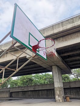 Empty sunlit basketball court in city park on hot sunny day under blue zenith sky. Bright sun in the sky. Sports, lifestyle, leisure activity concept