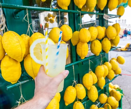 Caucasian hand with healthy fresh lemonade during summer with lemons background